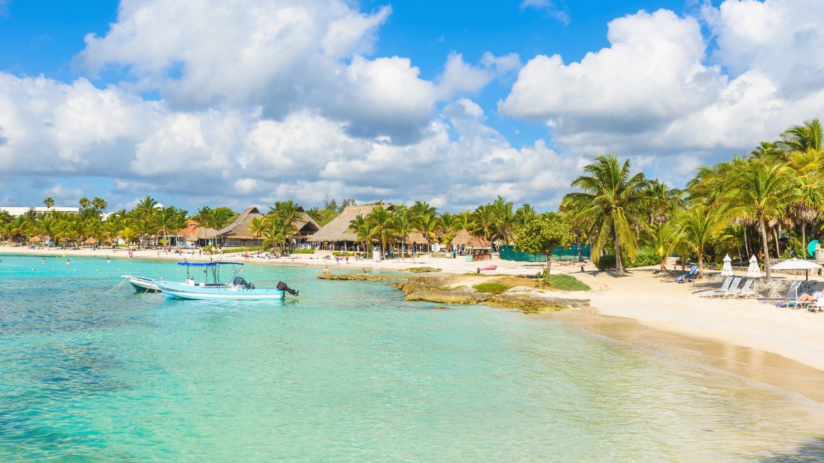 Baia di Akumal con barche ormeggiate nell'acqua turchese, sabbia bianca, palme e palapas sulla spiaggia